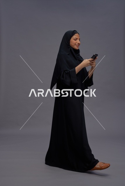 امرأة سعودية ترتدي عباءة تستخدم هاتف ذكي في استوديو