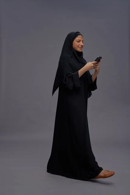 امرأة سعودية ترتدي عباءة تستخدم هاتف ذكي في استوديو