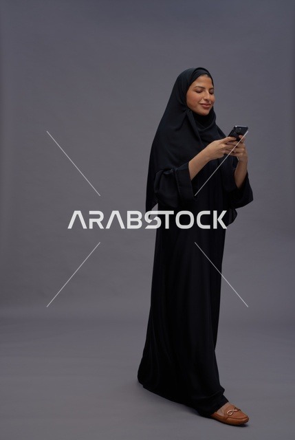 امرأة سعودية ترتدي عباءة تستخدم الهاتف الذكي في استوديو