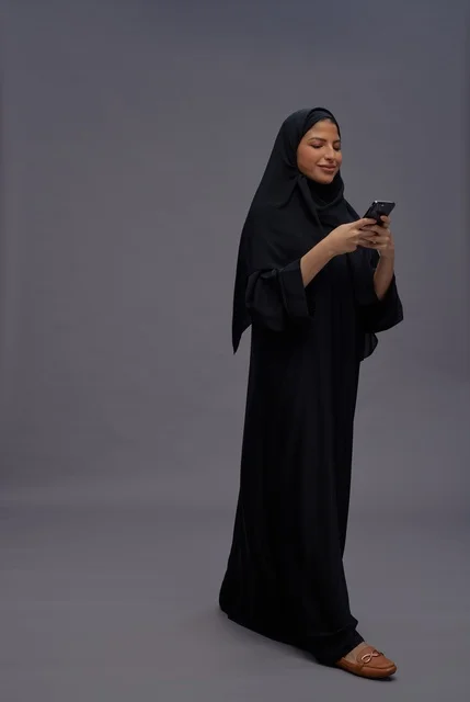امرأة سعودية ترتدي عباءة تستخدم الهاتف الذكي في استوديو