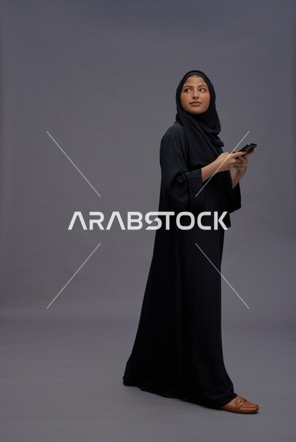 امرأة سعودية بالعباءة تستخدم هاتف ذكي في استوديو
