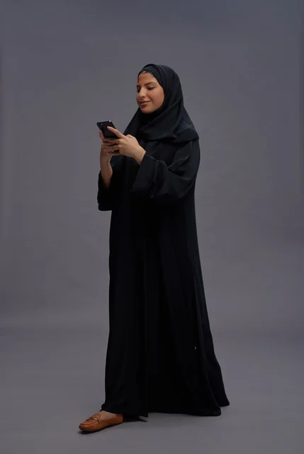 امرأة سعودية بالعباءة تستخدم الهاتف الذكي في الاستوديو