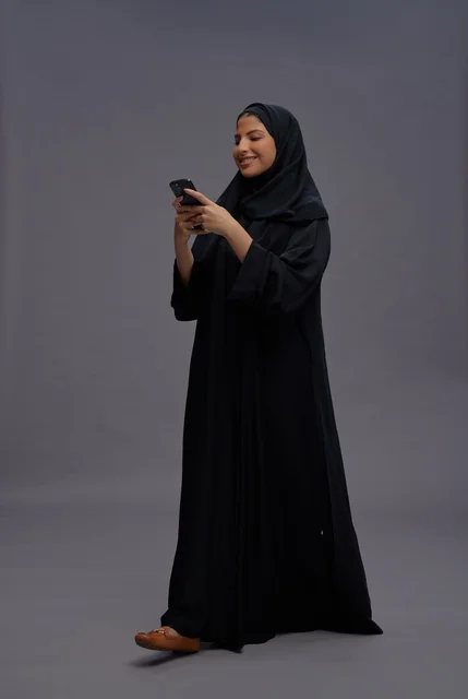 امرأة سعودية بعباءة تستخدم الهاتف الذكي في الاستوديو