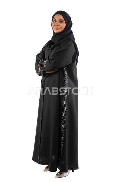 Portrait of a Saudi Arabian Gulf woman wearing a headscarf and black abaya standing straight with arms crossed, self-confidence, facial gestures indicating