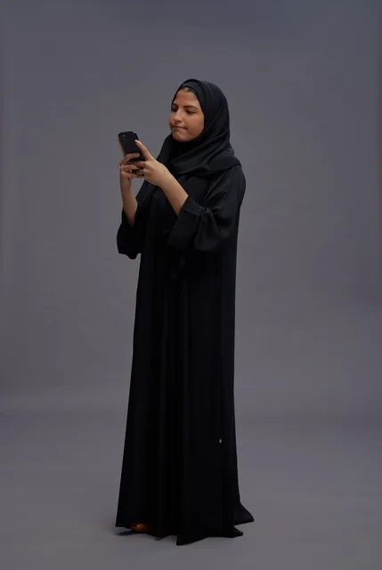امرأة سعودية بعباءة سوداء تستخدم الهاتف الذكي