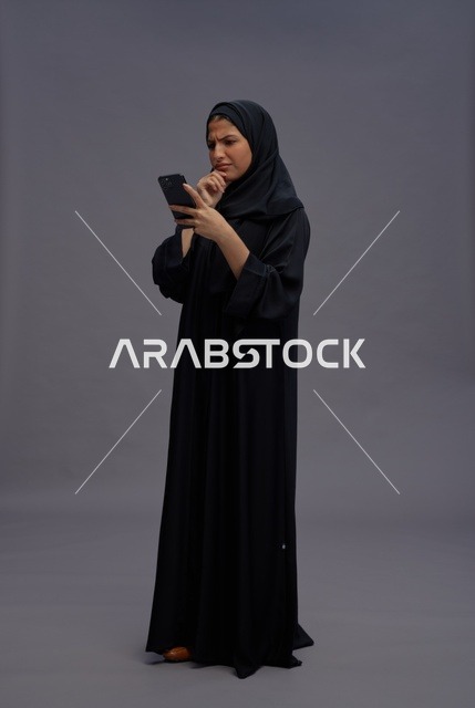 امرأة سعودية بالعباءة تستخدم الهاتف الذكي بتعبيرات حائرة