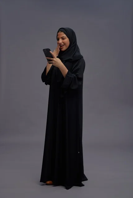 امرأة سعودية بالعباءة تستخدم الهاتف الذكي بتعجب