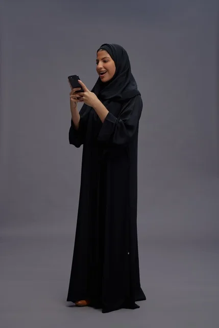 امرأة سعودية ترتدي عباءة وتستخدم الهاتف الذكي