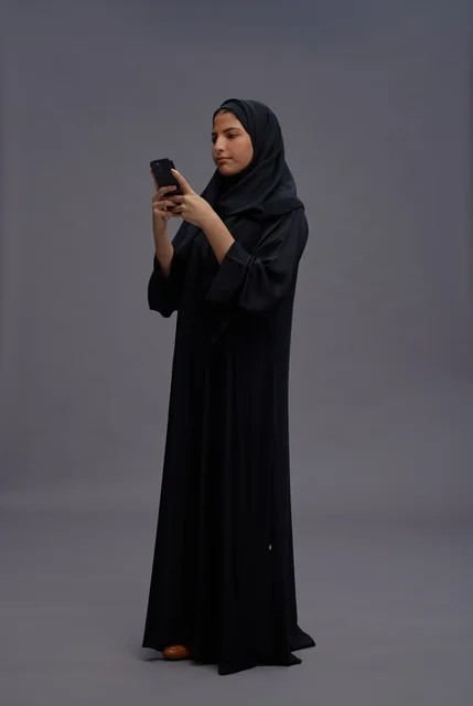 امرأة سعودية بالعباءة تستخدم الهاتف الذكي في الاستوديو