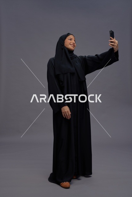 امرأة سعودية تلتقط صورة سيلفي بالهاتف الذكي والعباءة