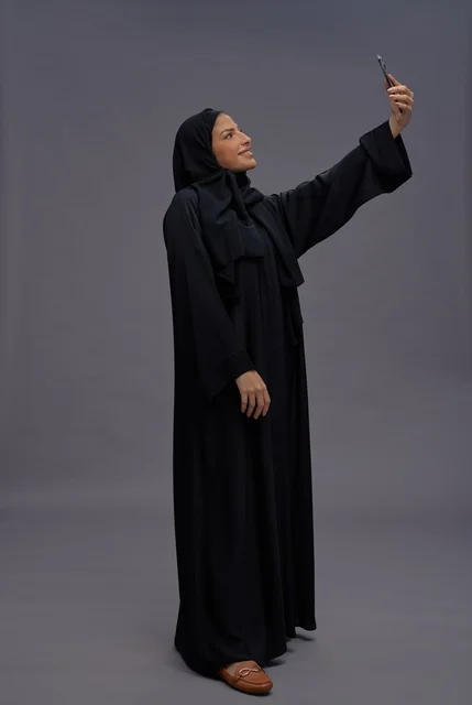 امرأة سعودية تلتقط سيلفي بالعباءة في استوديو خلفية رمادية