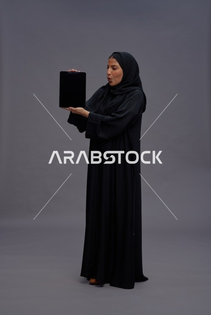 امرأة سعودية بالعباءة تحمل جهاز لوحي بشاشة فارغة
