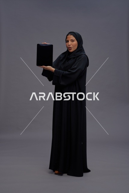 امرأة سعودية بالعباءة تمسك بجهاز لوحي بشاشة فارغة