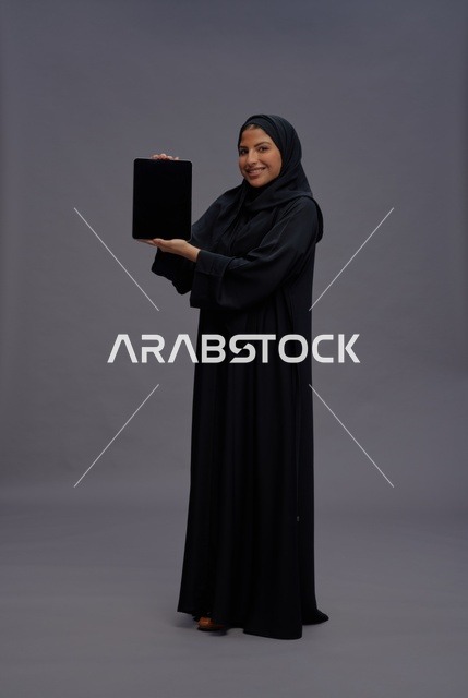 امرأة سعودية بالعباءة تمسك بجهاز لوحي بشاشة فارغة