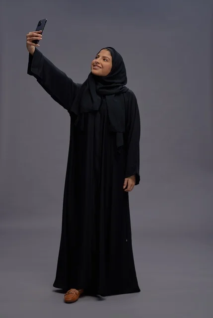 امرأة سعودية بالعباءة تلتقط صورة سيلفي بهاتف ذكي