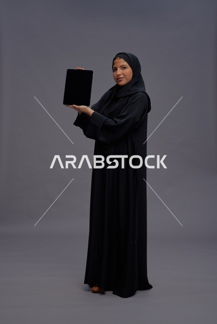 امرأة سعودية بعباءة تمسك بجهاز لوحي بشاشة فارغة