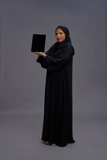 امرأة سعودية بعباءة تمسك بجهاز لوحي بشاشة فارغة