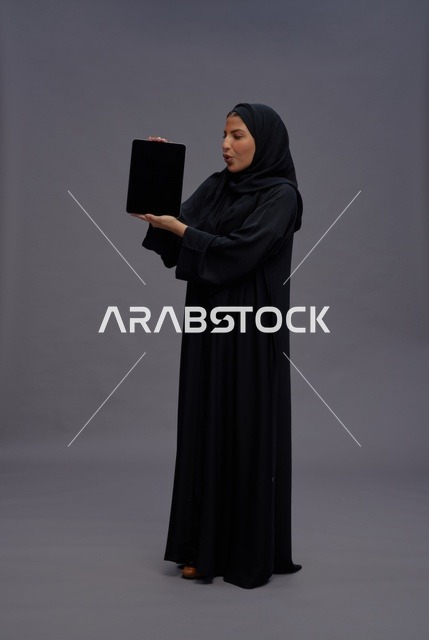 امرأة سعودية بالعباءة تحمل جهاز لوحي بشاشة فارغة