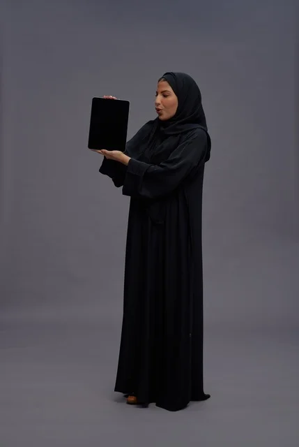 امرأة سعودية بالعباءة تحمل جهاز لوحي بشاشة فارغة امرأة سعودية بالعباءة تحمل جهاز لوحي بشاشة فارغة
