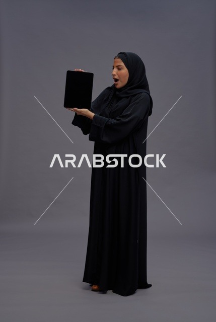 امرأة سعودية بالعباءة تمسك جهاز لوحي بشاشة فارغة