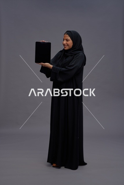 امرأة سعودية بالعباءة تحمل جهاز لوحي بشاشة فارغة