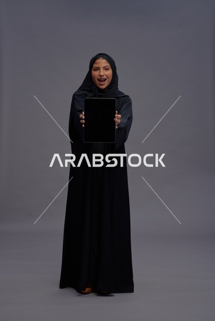 امرأة سعودية تمسك جهاز لوحي بشاشة فارغة في الاستوديو