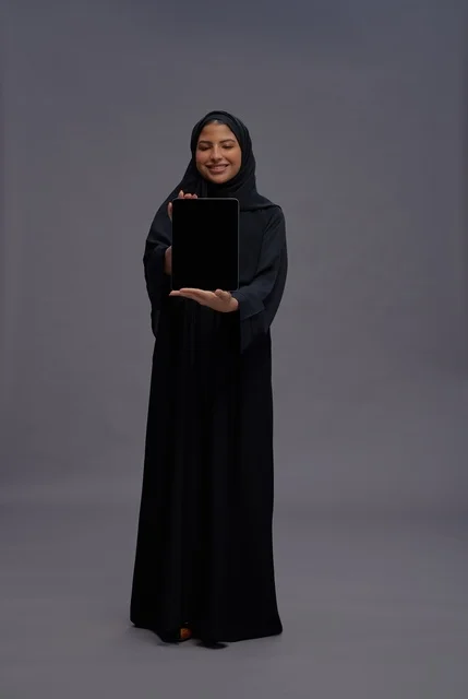 امرأة سعودية بالعباءة تمسك بجهاز لوحي شاشة فارغة