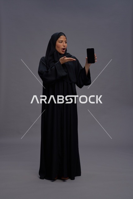 امرأة سعودية بالعباءة تمسك هاتف ذكي بشاشة فارغة
