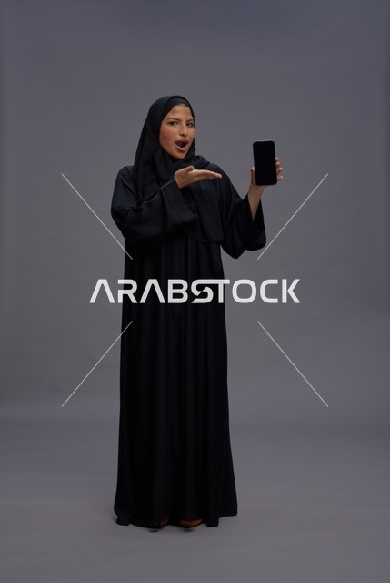 امرأة سعودية بعباءة سوداء تمسك هاتف ذكي بشاشة فارغة