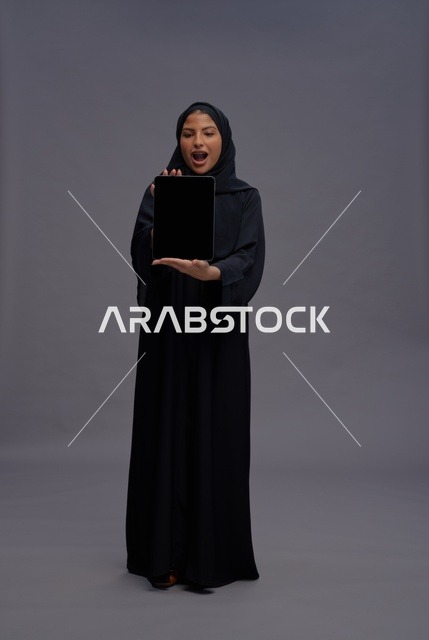 امرأة سعودية بالعباءة تمسك جهاز لوحي شاشة فارغة