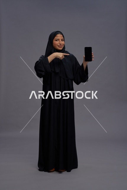 امرأة سعودية بالعباءة تمسك هاتف ذكي بشاشة فارغة