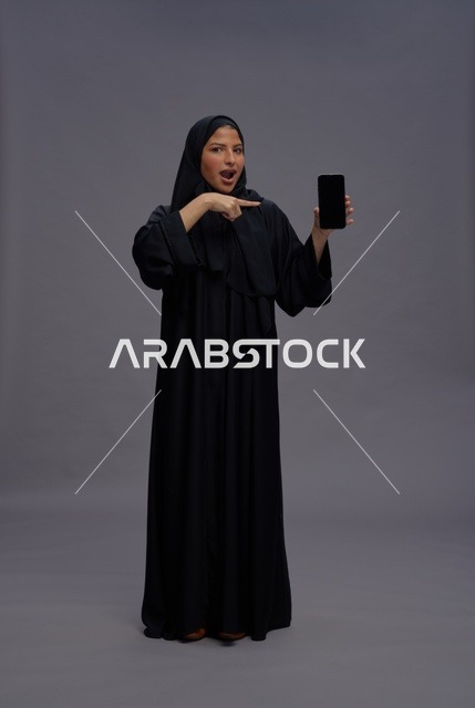 امرأة سعودية بالعباءة تشير إلى شاشة هاتف ذكي فارغة