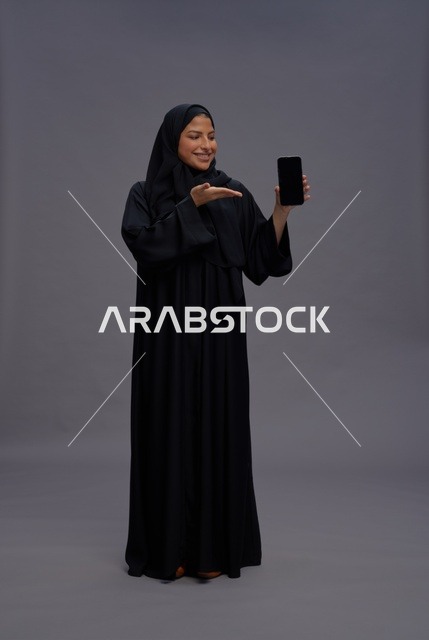 امرأة سعودية بالعباءة تمسك هاتف ذكي بشاشة فارغة