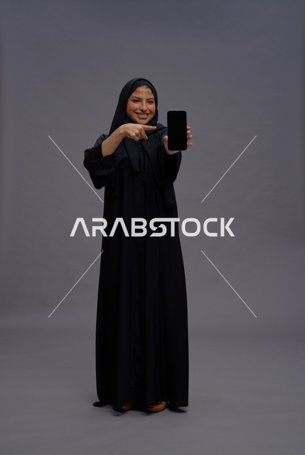 امرأة سعودية بالعباءة تشير إلى شاشة هاتف ذكي