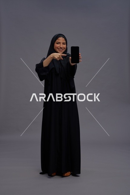 امرأة سعودية بالعباءة تمسك هاتف ذكي بشاشة فارغة