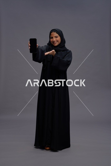 امرأة سعودية بالعباءة تمسك هاتف ذكي بشاشة فارغة