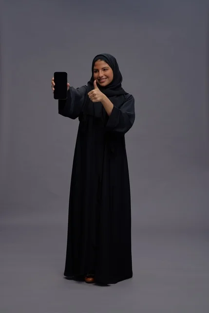 امرأة سعودية مع هاتف ذكي وإيماءة الإبهام تصوير استوديو