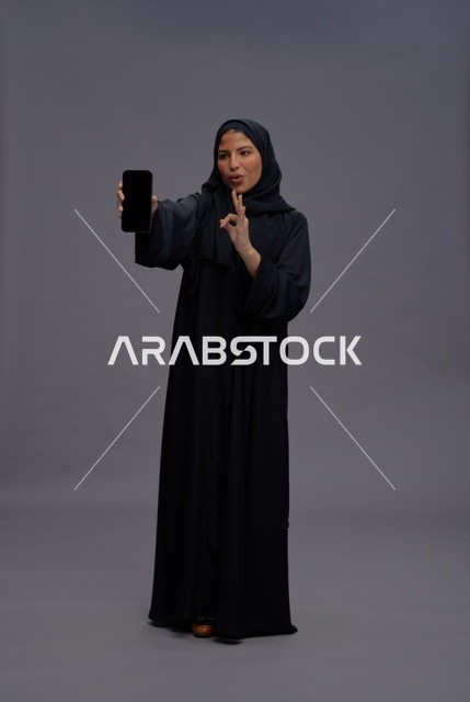 امرأة سعودية بعباءة تمسك هاتف ذكي بشاشة فارغة