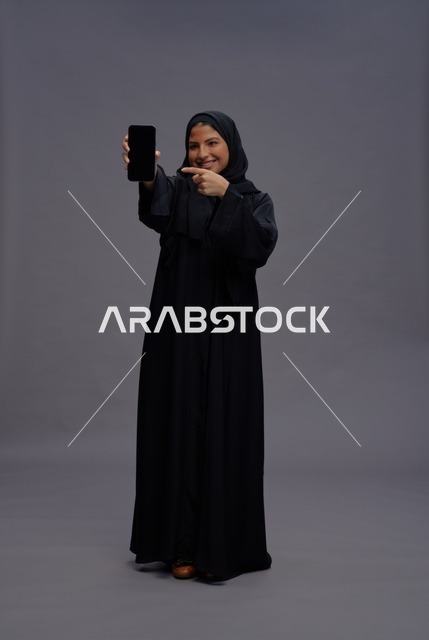امرأة سعودية بالعباءة تشير لشاشة هاتف ذكي