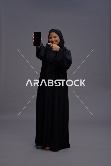امرأة سعودية بعباءة تشير إلى شاشة هاتف ذكي