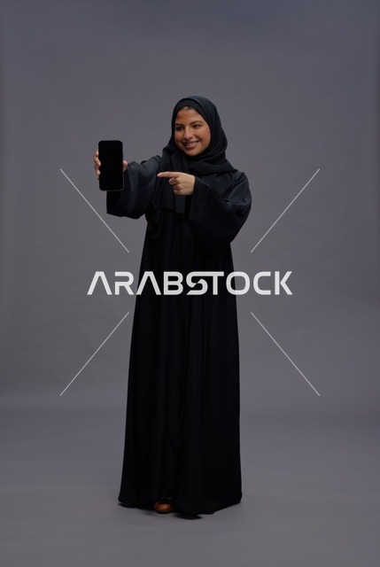 امرأة سعودية بعباءة تشير إلى شاشة هاتف ذكي