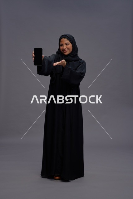 امرأة سعودية بالعباءة تمسك هاتف ذكي بشاشة فارغة