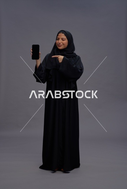 امرأة سعودية بالعباءة تشير إلى شاشة هاتف ذكي