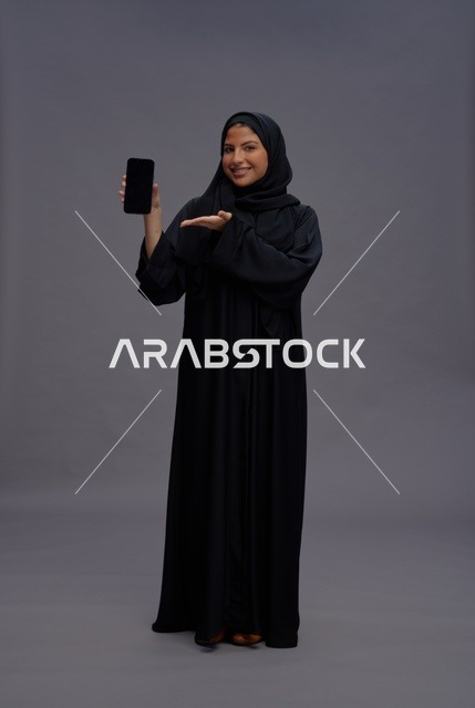 امرأة سعودية بعباءة تمسك هاتف ذكي بشاشة فارغة