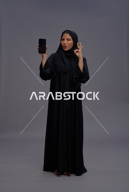 امرأة سعودية بالعباءة تمسك هاتف ذكي بشاشة فارغة