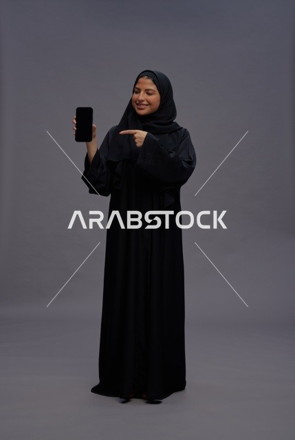 امرأة سعودية بالعباءة تشير إلى شاشة هاتف ذكي