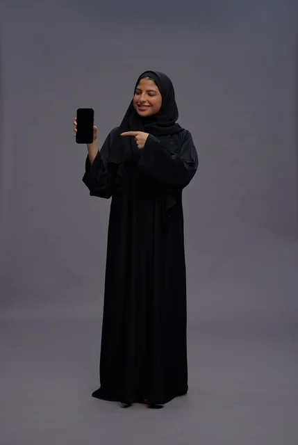 امرأة سعودية بالعباءة تشير إلى شاشة هاتف ذكي