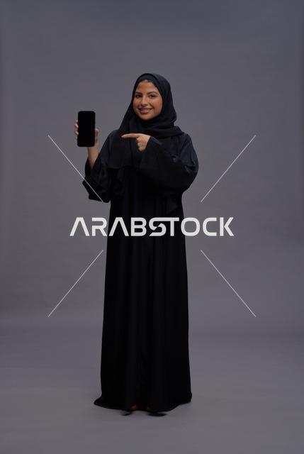 امرأة سعودية بالعباءة تشير لشاشة هاتف ذكي