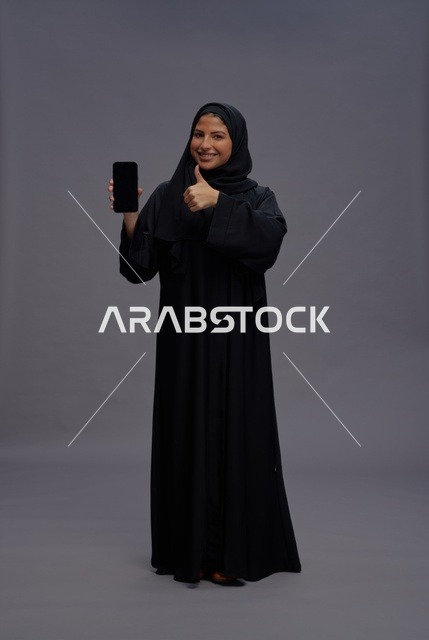 امرأة سعودية بالعباءة تحمل هاتف ذكي وتشير بالإعجاب