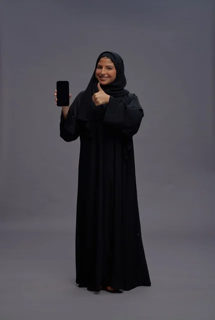 امرأة سعودية بالعباءة تحمل هاتف ذكي وتشير بالإعجاب
